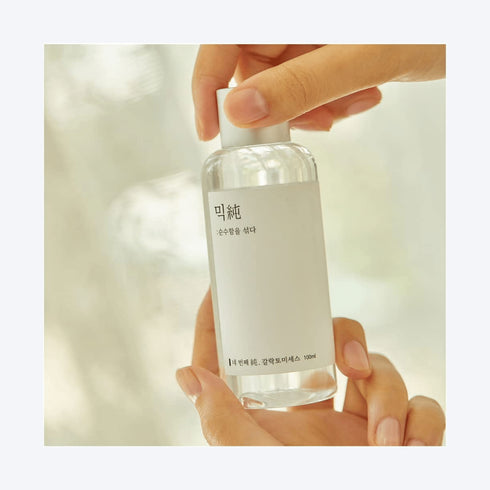 MIXSOON Galactomyces Ferment Essence Imaginea înfățișează o mână care ține cu grijă o sticlă de Mixsoon's Beta-Glucan Face Essence. Acest produs este o dovadă a angajamentului mărcii față de minimalism și eficacitate. Flaconul transparent și eticheta curată a esenței reflectă puritatea și simplitatea formulei din interior